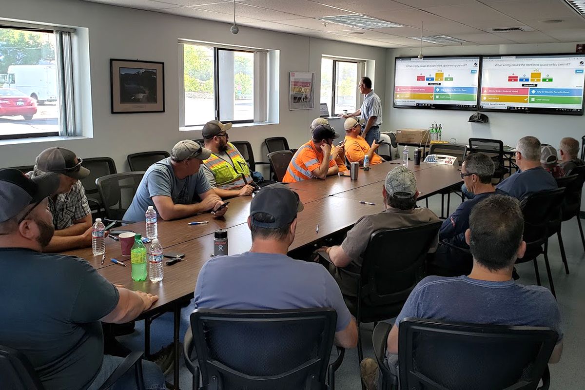 a group of men sit around a table with a man giving a presentation