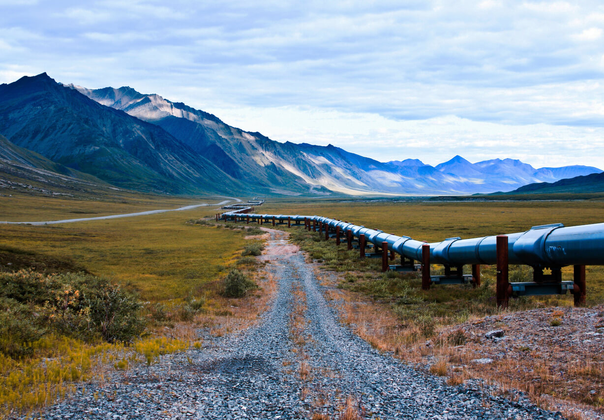 a pipeline runs through a grassy field with mountains in the background