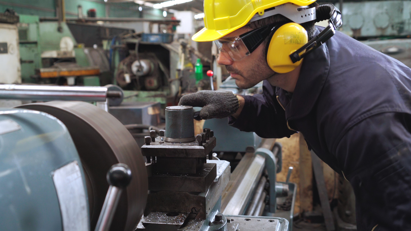 a man wearing a hard hat and ear protection works on a machine