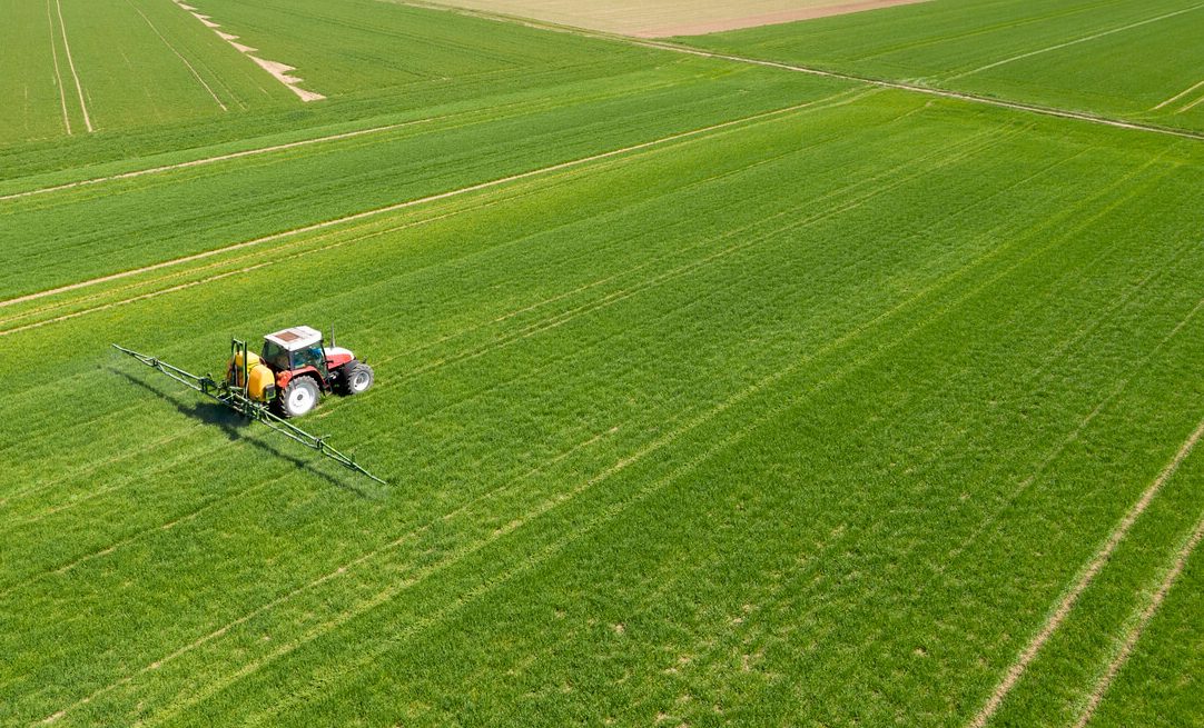 an aerial view of a tractor spraying a field of grass