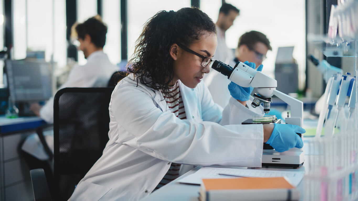 a woman in a lab coat looks through a microscope