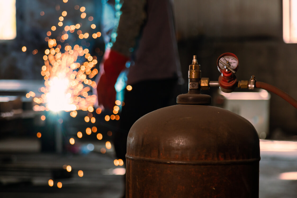 a man is welding a piece of metal with a propane cylinder in the foreground