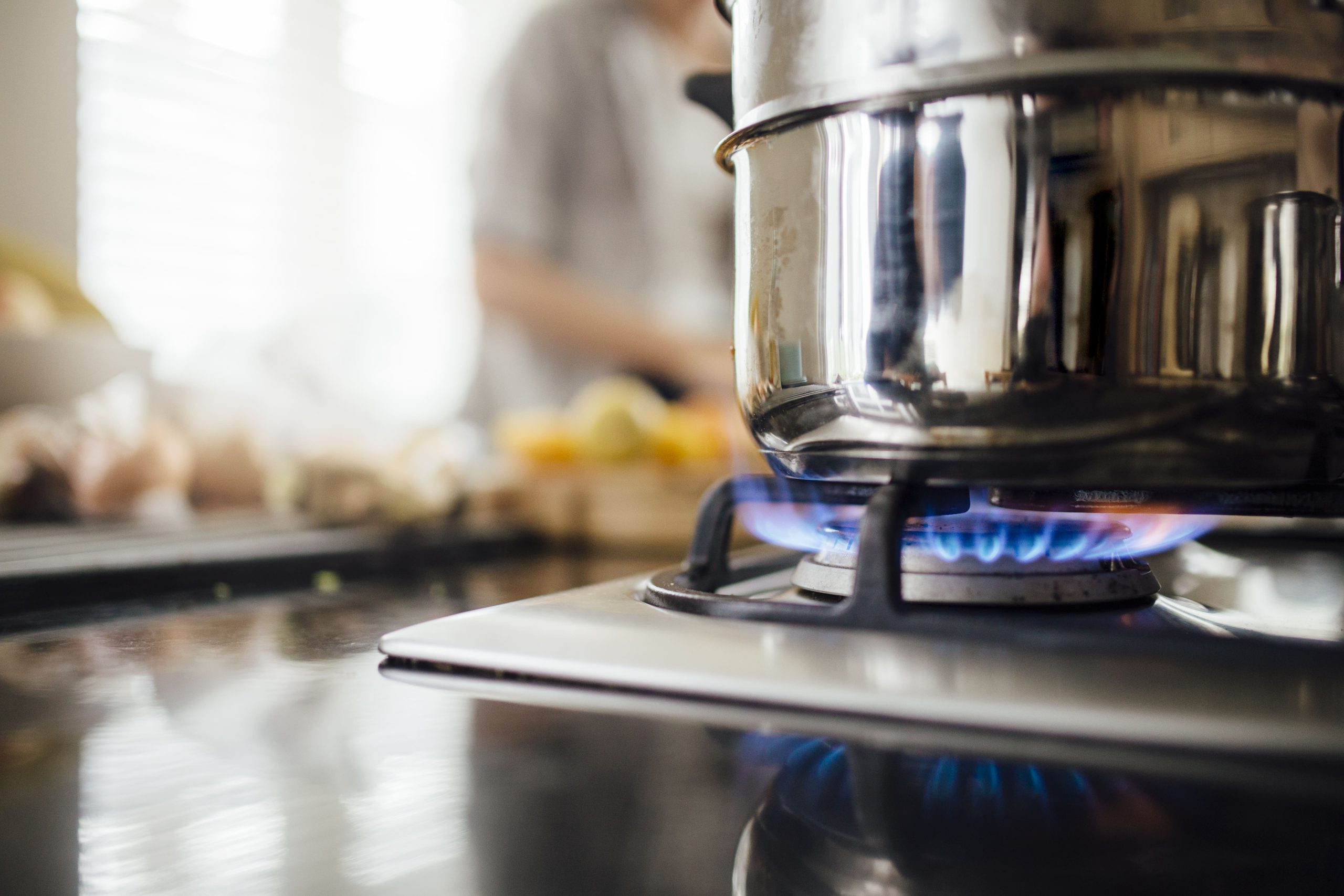 a pot is cooking on a gas stove with a person in the background