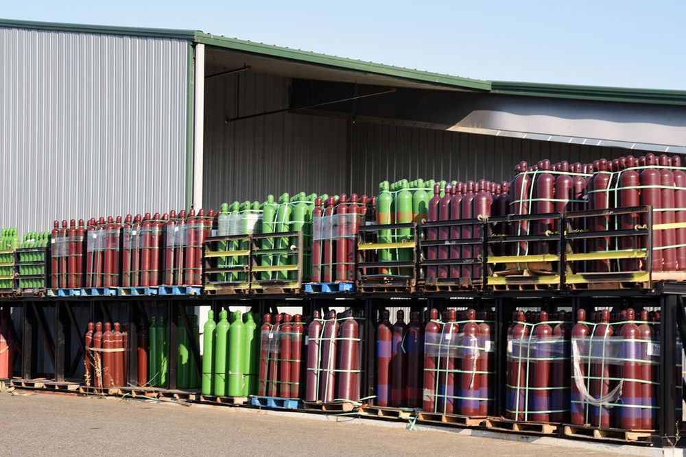 a bunch of gas cylinders are stacked on pallets outside of a building