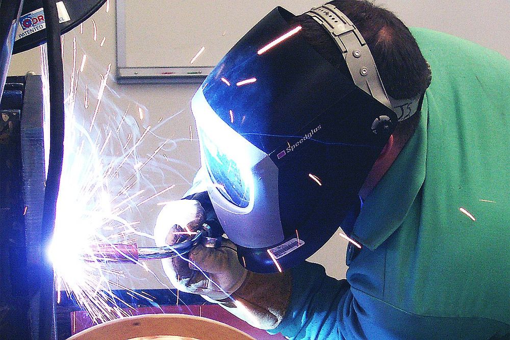 a man wearing a speedglas welding mask is welding a piece of metal