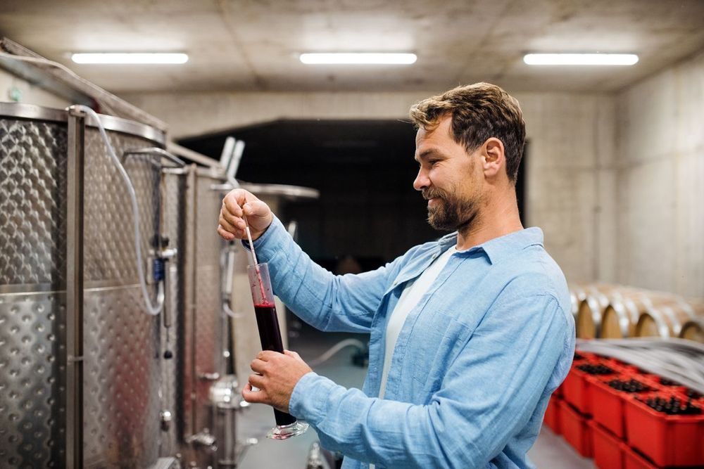 a man in a blue shirt is pouring red liquid into a glass