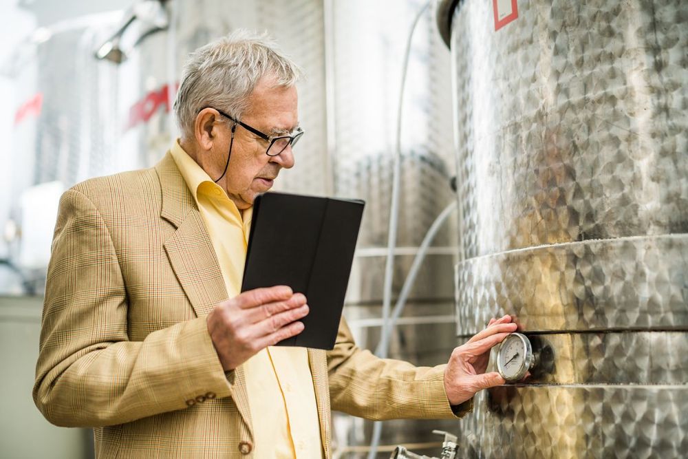 a winemaker looks at a thermometer while holding a tablet