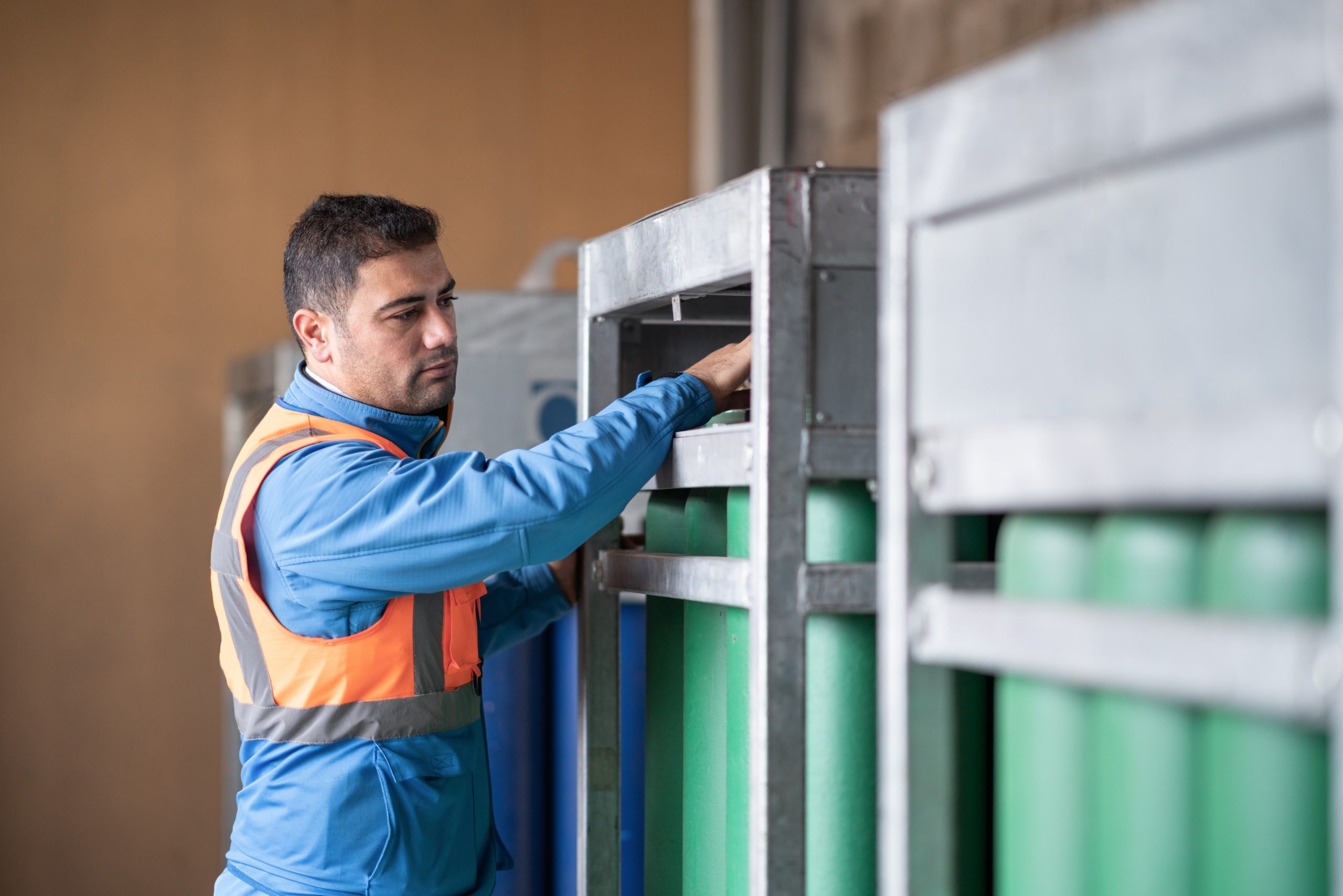 a man in a blue jacket and orange vest is looking at a green cylinder