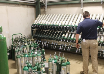 a man in a blue shirt stands in a room full of oxygen cylinders