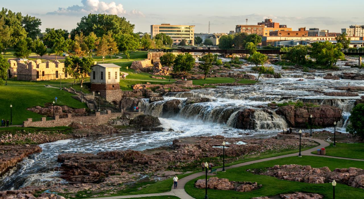 a waterfall in a park in Sioux Falls, SD with buildings in the background