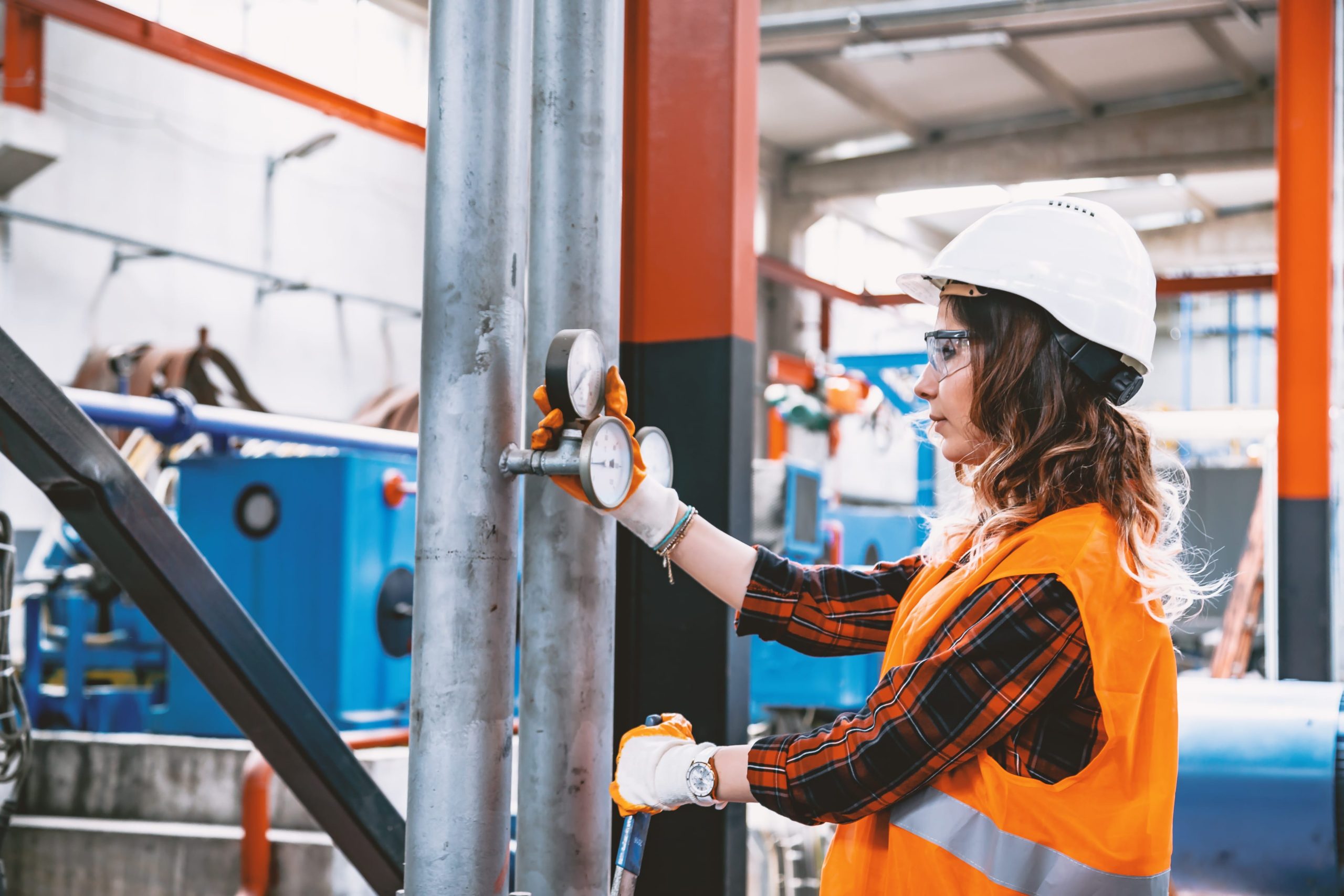 a woman wearing a hard hat and safety vest is working on a pipe