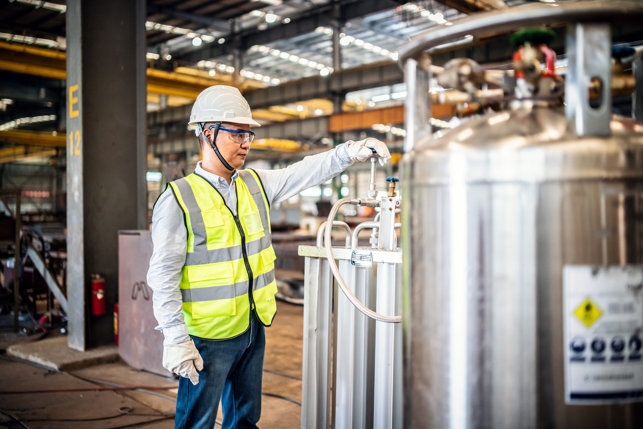 a man wearing a hard hat and safety vest is working in a factory