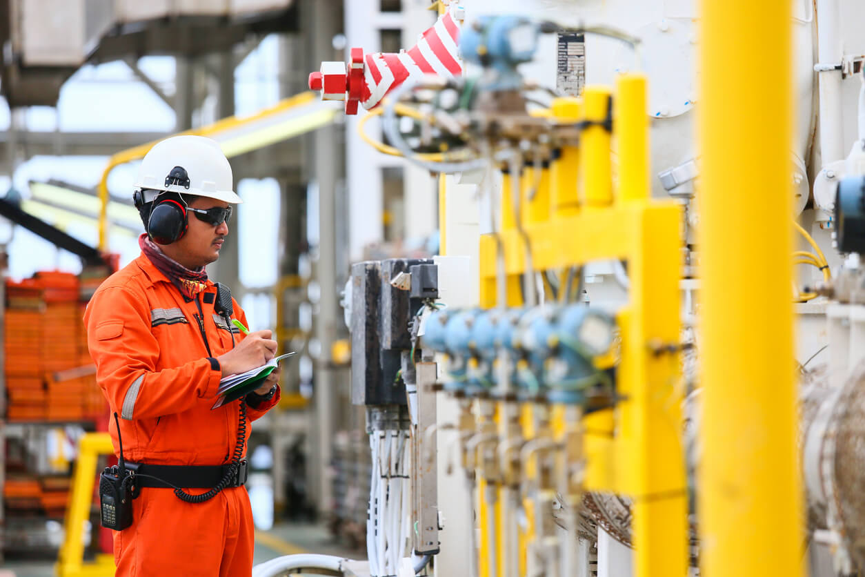 a man wearing a hard hat and orange overalls is writing on a clipboard